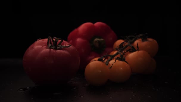 Tomate vermelho orgânico fresco, cereja amarela e pimentão vermelho com gotas de água em um fundo preto. A iluminação muda de tecla alta para tecla baixa. Alimentação saudável — Vídeo de Stock