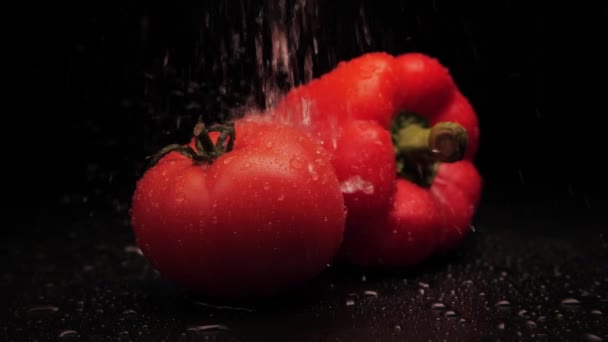 Tomate rouge bio fraîche lavée et poivron rouge avec des gouttes d'eau sur un fond noir. Gros plan d'un puissant jet d'eau à la surface des légumes. Une alimentation saine — Video