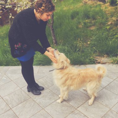 Beyaz bir kadın bahçede evcil hayvanıyla oynuyor.