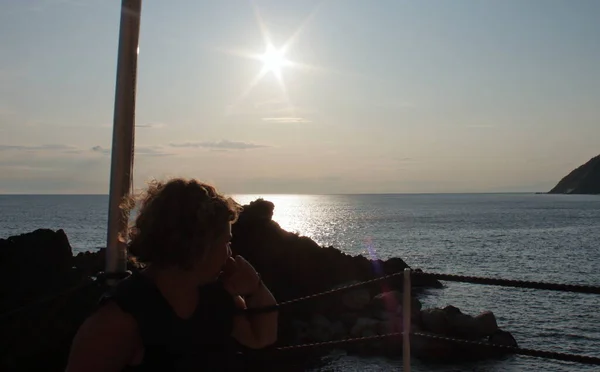 Una rubia caucásica mirando un velero en el horizonte durante el atardecer en el bar de la playa — Foto de Stock