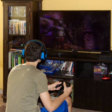 Kulaklıklı, koltukta oturan, konsolla video oyunu oynayan beyaz bir çocuk.