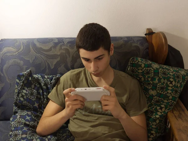 Kaukaski chłopiec bawi się przenośną konsolą na kanapie — Zdjęcie stockowe
