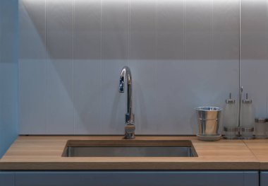 Modern musluk, paslanmaz lavabo ve mutfaktaki gri renkli duvar iç dekorasyonlu şişeler.