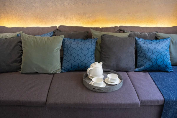 現代的な茶色 青のチェック柄のグループは 紫色のクッションの服のソファにコーヒーカップのセットと装飾コンセプトのインテリアの後ろから黄色のライトと壁の生地の枕を着色します — ストック写真