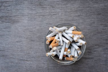 Kül tablasında sigara izmaritleri, ahşap masa üzerinde yazılı yer, sigara içme alanı kavramı, sigara kirliliği.