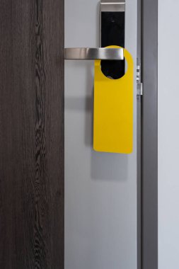 Oda sarı etiketli otel tabelası modern metal kapı kolunda asılı çalışma alanı olan ahşap kapı kolunda otel odasının kapalı kapısı.