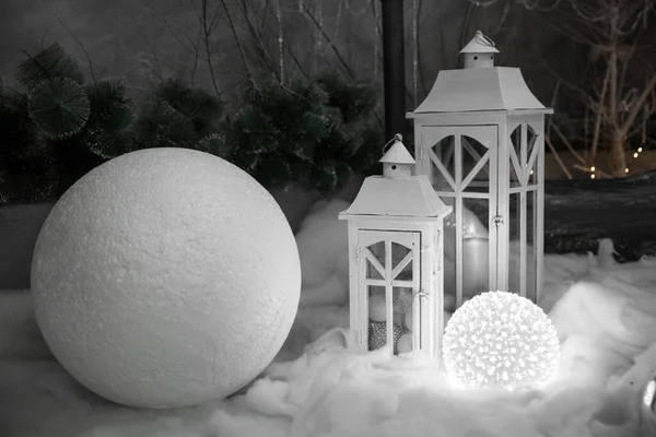 İki beyaz ahşap fener ve büyük mavi top çelengi ile aydınlatılmış karanlık bir ormanda yapay kar üzerinde dev bir kartopu standı. Noel ve sihir kavramı, metin için bir yer..