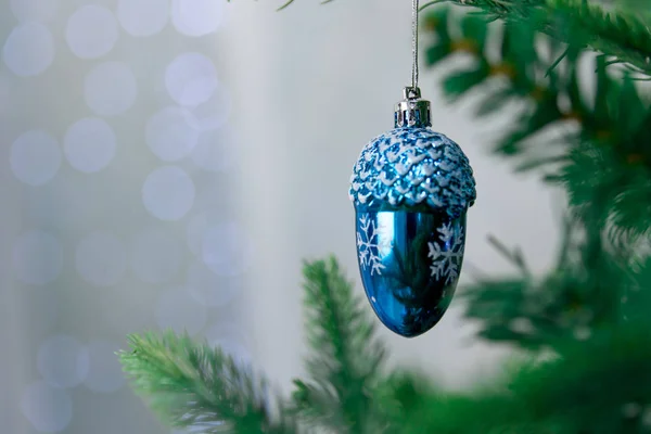 Close-up-Weihnachtsdeko-Christbaumkugel, Tannenzapfen blau, die an einem grünen Weihnachtsbaum auf dem Hintergrund von Bokeh hängen. Neujahr Winter Hintergrund. — Stockfoto