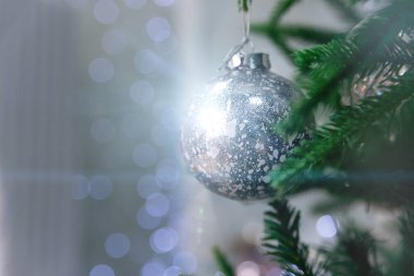 Güzel bir Noel süslemesi yakın plan. Mavi Bokeh 'in arka planındaki Noel ağacında asılı gümüş bir Noel topu. Noel arkaplanı Bokeh ve sihirli röflelerle.