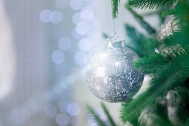Güzel bir Noel süslemesi yakın plan. Mavi Bokeh 'in arka planındaki Noel ağacında asılı gümüş bir Noel topu. Noel arkaplanı Bokeh ve sihirli röflelerle.