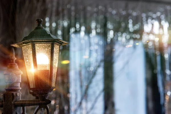 Antique frosty lamppost with orange light on the street close up on the background of the window in shining Christmas decorations sequins. Vintage glass light in night city. — Stock Photo, Image