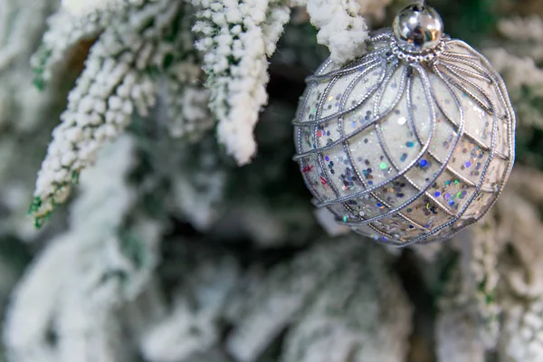 Κοντινό πλάνο της όμορφης χριστουγεννιάτικης διακόσμησης - μπιχλιμπίδι ασημένια μπάλα κρέμεται στο χριστουγεννιάτικο δέντρο στο φόντο των καλυμμένων με χιόνι κλαδιά. Ασημί μπεζ Χριστούγεννα χειμώνα φόντο — Φωτογραφία Αρχείου