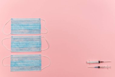 Tıbbi maskeler ve şırıngalar pembe arka planda yatar. Koronavirüs virüslerine karşı korunma ve soğuk algınlığının önlenmesi ve tedavi önerileri.