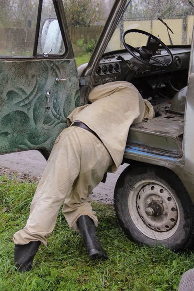 Ein Mann in Overalls versucht, ein altes kaputtes Auto zu reparieren. Der Stil Stalker. — Stockfoto