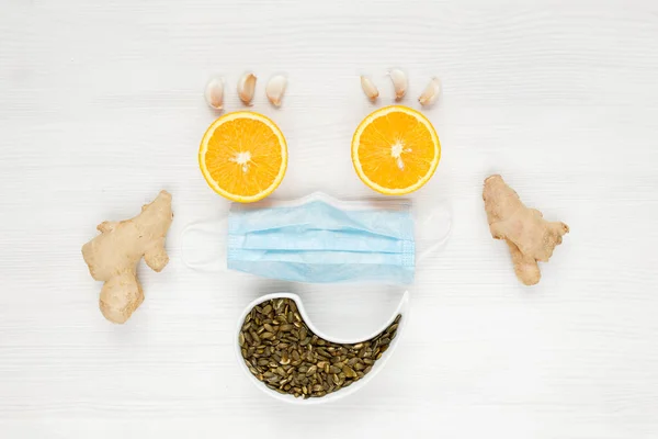 Tıbbi maske takan meyve ve tohumların mutlu yüzü. Gülen yüz portakal, sarımsak, zencefil ve balkabağı tohumlarından yapılır. Yararlı antiviral ürünlerin arka planı