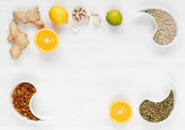 Portakal, zencefil, sarımsak, ıhlamur, limon, kuru üzüm, ayçiçeği çekirdeği, kabak tohumları beyaz ahşap bir yüzeyde uzanıyor. Organik, vejetaryen ürünler vücudun bağışıklığını arttırır.