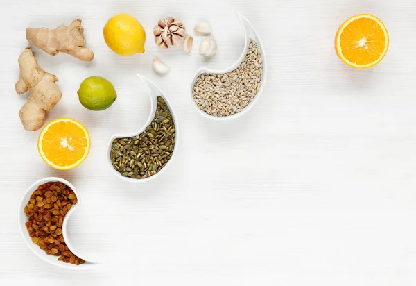 Doğal sağlıklı ürünler. Portakal, zencefil, sarımsak, ıhlamur, limon, kuru üzüm, ayçiçeği çekirdeği, balkabağı tohumları beyaz ahşap bir yüzeyde uzanır.