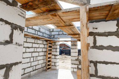 İnşaat halindeki bir evin inşaatı. Beyaz havalandırmalı beton bloklardan yapılmamış ev duvarları. Yönetim kurulları ve Avrupa paletlerinden toplanan işçilerin yapı iskelesi