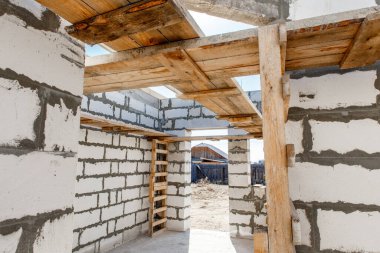 İnşaat halindeki bir evin inşaatı. Beyaz havalandırmalı beton bloklardan yapılmamış ev duvarları. Yönetim kurulları ve Avrupa paletlerinden toplanan işçilerin yapı iskelesi