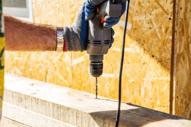 Bir işçi ahşap bir çubukta bir matkapla delik açıyor. Elektrikli matkapla ahşap matkap. İnşaat arkaplanı