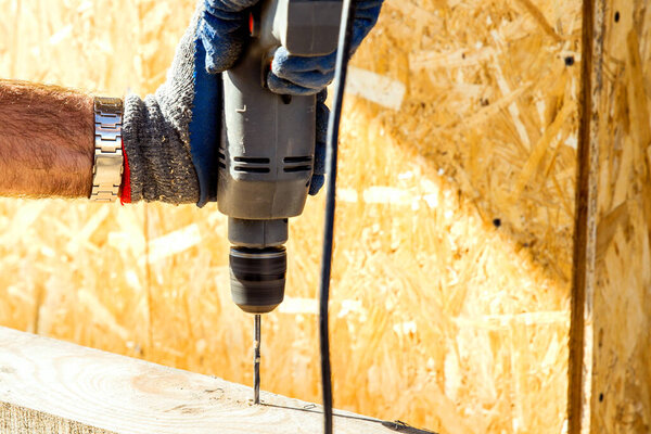 A worker drills a hole in a wooden bar with a drill on wooden. Wooden bar drilling with an electric drill. Construction background