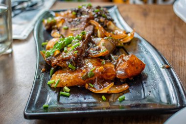 Huysuz arka planda siyah tabakta servis edilen kızarmış acılı domuz eti. Seçici odak