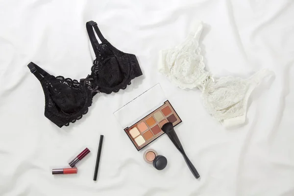 Make-up products with black and white bras on white background. Top view, white bedding on lipstick, brush and colorful makeup products - Image