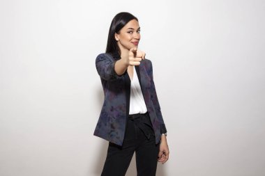 Güzel, uzun saçlı esmer kadın stüdyoda kamerayı işaret ediyor.