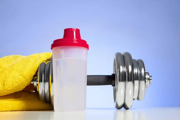 Dumbbell and whey protein shaker on a blue towel surface. Sports bodybuilding supplements or nutrition. Fitness or healthy lifestyle concept.