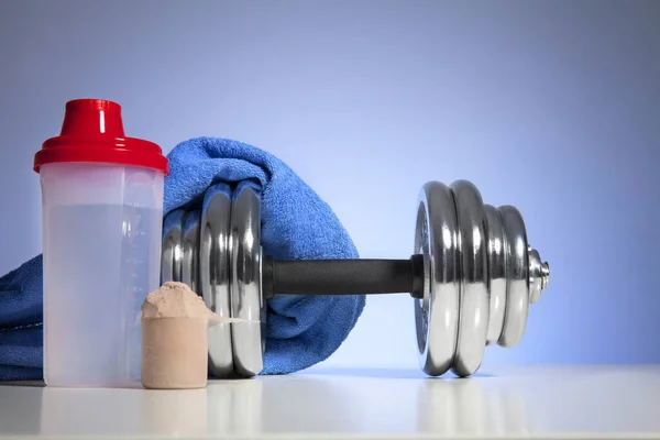 Dumbbell and whey protein shaker on a blue towel surface. Sports bodybuilding supplements or nutrition. Fitness or healthy lifestyle concept.