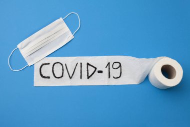 Coronavirus salgını covid 19 tuvalet kağıdı rulosu ve mavi arka planda tek kullanımlık yüz maskesi üzerine yazılmış..