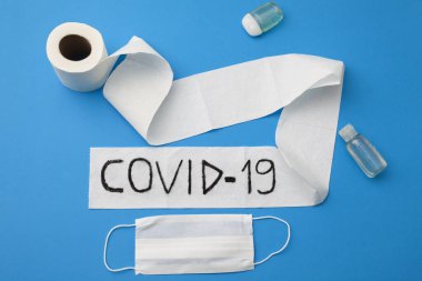 Coronavirus salgını. Tuvalet kağıdı rulosu, el dezenfektanı ve mavi arka planda tek kullanımlık yüz maskesi üzerine yazılmış..