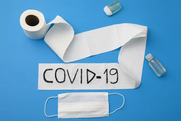 Coronavirus salgını. Tuvalet kağıdı rulosu, el dezenfektanı ve mavi arka planda tek kullanımlık yüz maskesi üzerine yazılmış..
