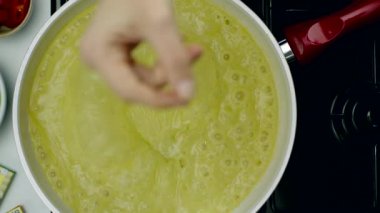 Kadının eli çorbaya baharatlı zar atıyor.