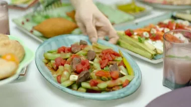 Kadın geleneksel taze fasulye servis ediyor. Yemek masasında domates ve etle pişiriliyor..