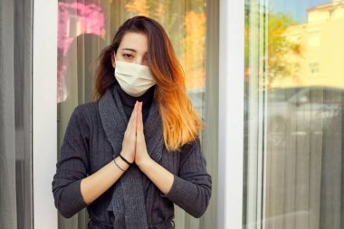 Sick woman staying at home and praying for protection from coronavirus wearing a disposable medical mask on her face. clipart