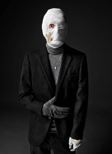 Strange looking injured man in black turtleneck sweater and suit, his head wrapped up with bandages.