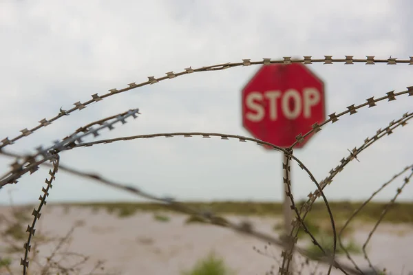 Red stop sign behind safety fence of barbed wire — Stock Photo, Image