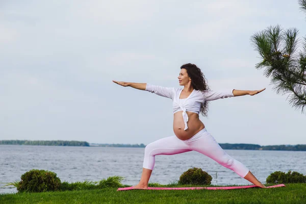 O femeie însărcinată practică yoga lângă râu — Fotografie, imagine de stoc