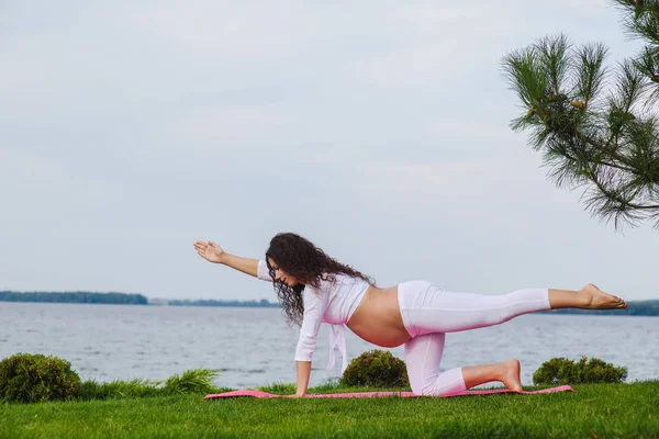 O femeie însărcinată practică yoga lângă râu — Fotografie, imagine de stoc
