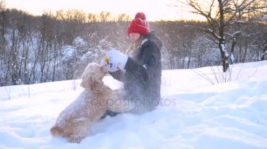 Sevimli kız kırmızı şapka ve onu köpek kelepçelememz ve kış arka plan dalga. Bir sprey kar gel kız ve onun cocker spaniel açık havada oynamak için