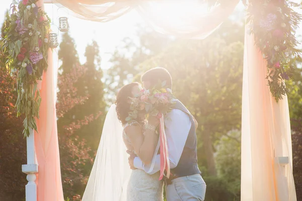 Feliz pareja besándose bajo el arco textil —  Fotos de Stock