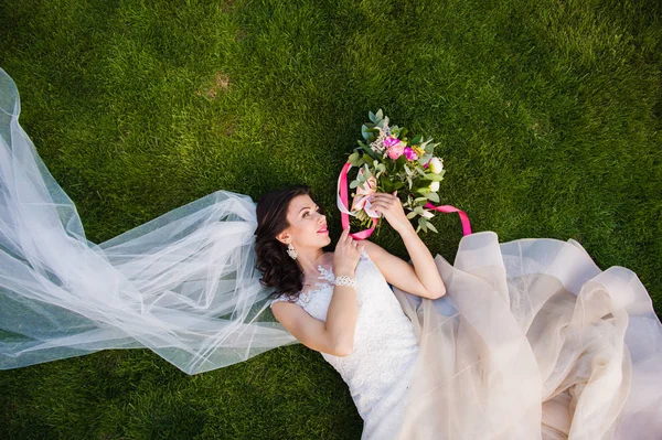 Beautiful brunette bride lying in the grass — Stock Photo, Image