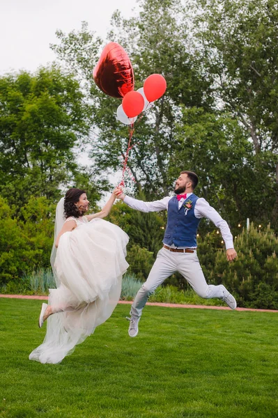 Felice coppia sposata saltando con palloncini rossi — Foto Stock