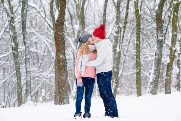 Romantic couple in knitted hats going to kiss during snowfall — Stock Photo, Image