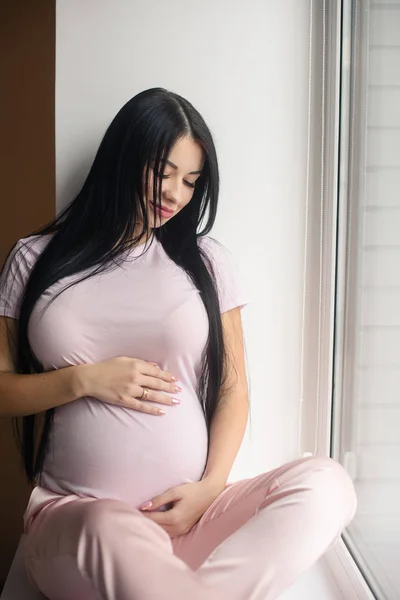 Portrait of smiling pregnant woman sit in window sill