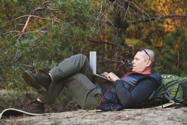 Sırt çantalı turist dizüstü bilgisayarla mindere uzanıyor