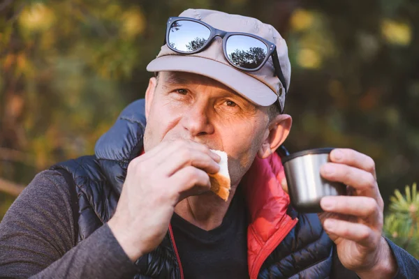 Elderly hiker eating a sandwich and drinking