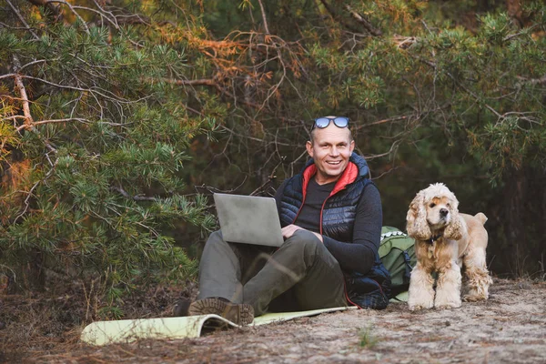 Äldre turist med laptop och hund i skogen — Stockfoto