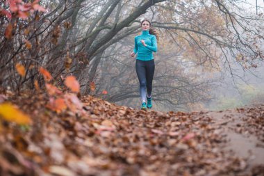 Parkta mavi spor kıyafetlerle koşan bir kadın.
